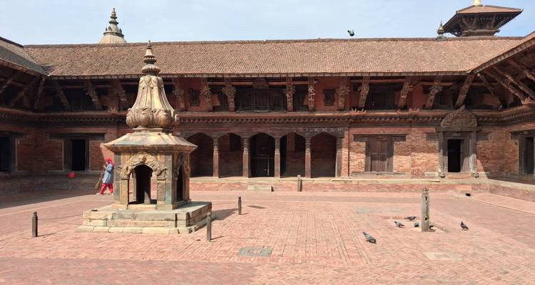 Quiet inner courtyard of Bhaktapur with stone fountain and pigeons on red-brick ground.
