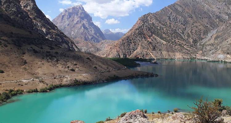 Lac turquoise brillant entouré de montagnes rocheuses escarpées sous un ciel d'été lumineux.