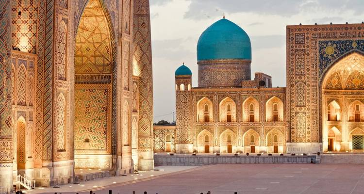 Le dôme turquoise illuminé et les murs ornés de la médersa brillent au crépuscule dans une grande place.