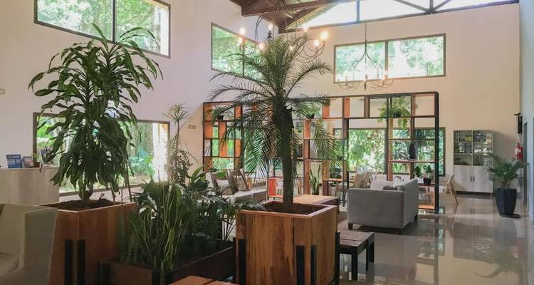 Stijlvolle hotellobby vol met groene planten en grote ramen met uitzicht op jungle.