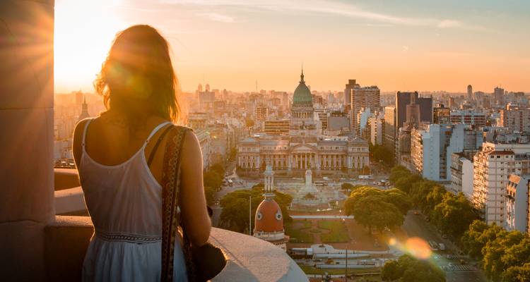 Vrouw die naar de zonsondergang boven Buenos Aires kijkt vanaf een hoog terras, met de glinsterende stadshorizon eronder.