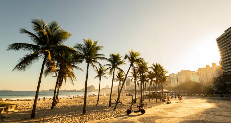 Gouden verlichte strandpromenade van Ipanema omzoomd met palmbomen in de late namiddag.