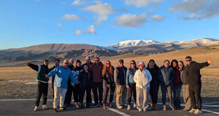 Groupe de touristes posant ensemble avec des montagnes enneigées au loin et de vastes plaines en arrière-plan.
