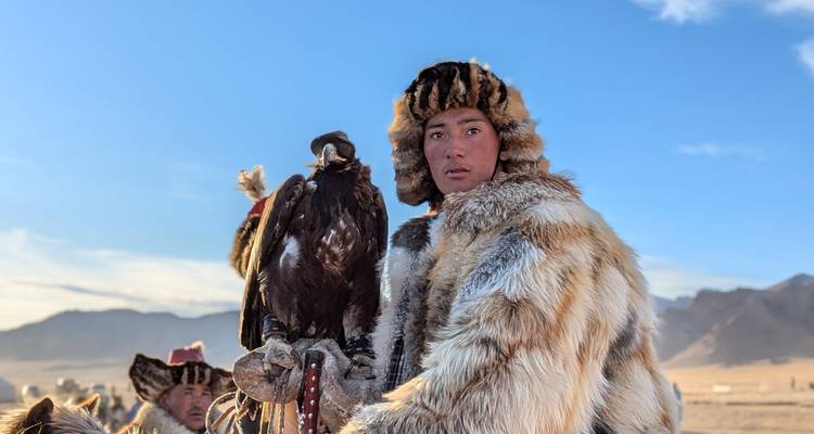 Portrait en gros plan d'un chasseur à l'aigle en manteau de fourrure tenant son aigle royal au lever du soleil.
