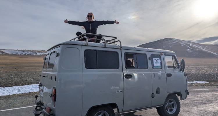 Voyageur se tenant triomphalement au sommet d'un van robuste dans un paysage grand ouvert.