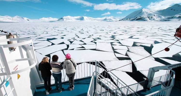 Reizigers die op het dek van een schip staan en uitkijken over een uitgestrekt veld van gebroken zee-ijs.