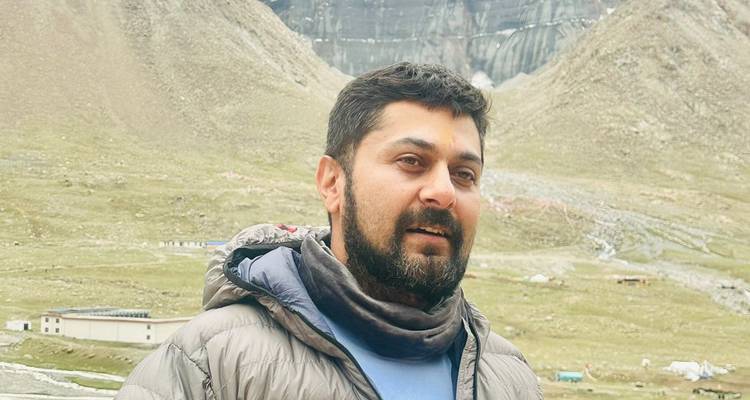 Portrait d'un randonneur en veste et cache-cou debout devant les pentes dénudées de l'Himalaya et les glaciers.