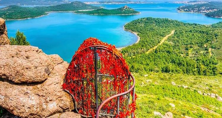 Türkisfarbener Küstensee und grüne Inseln, betrachtet von einem felsigen Aussichtspunkt, der mit einem roten herzförmigen Metallrahmen geschmückt ist