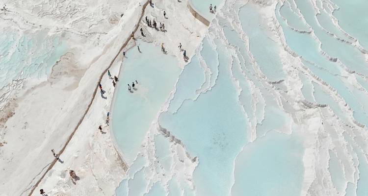 Luftaufnahme der weißen Travertinterrassen und blauen Becken von Pamukkale mit Besuchern, die entlang der seichten Gewässer wandeln