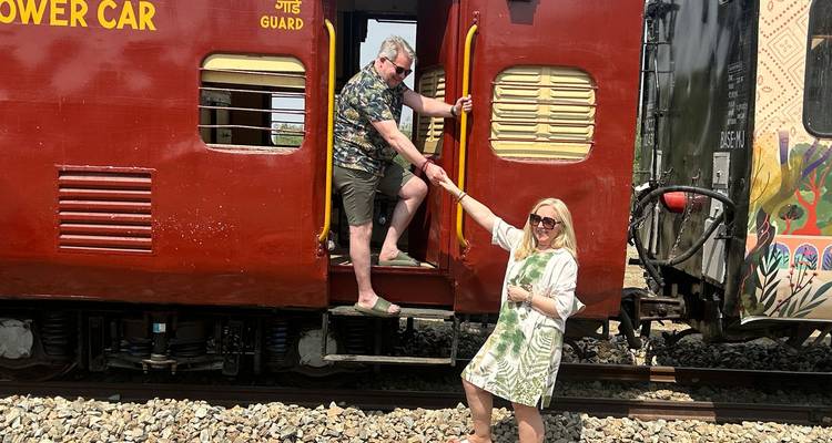 Man helpt vrouw om af te stappen van een rode Indische treinwagon op spoorlijnen.