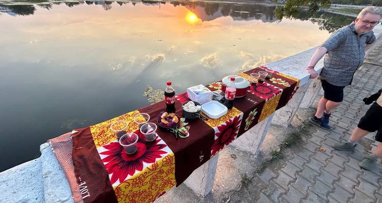 Tafel met picknicksnacks en drankjes met uitzicht op reflecterend meer bij zonsondergang.