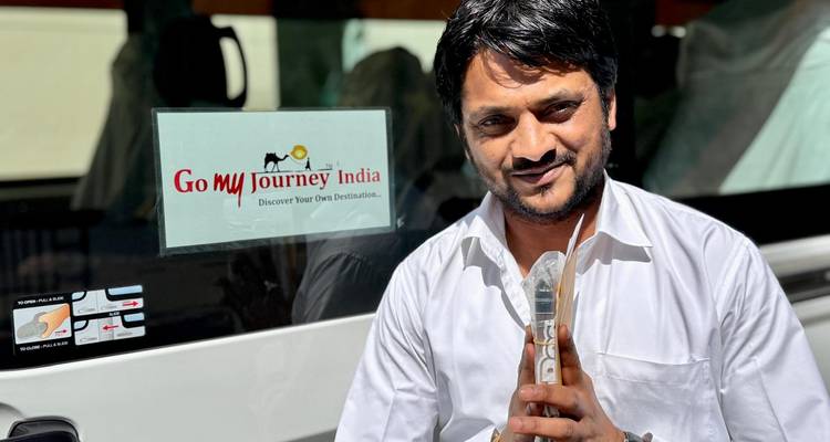 Chauffeur met een kleine trofee in de hand staat bij een tourbus met 'Go my Journey India' logo.