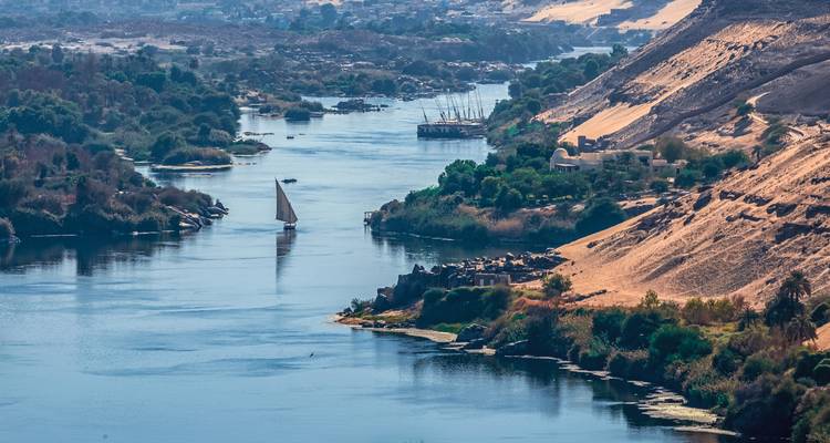 Étendue sereine du Nil serpentant entre des îles verdoyantes et des rives désertiques dorées avec un voilier solitaire