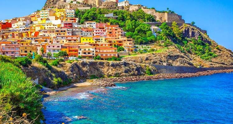 Lebendige Terrassenstadt, gekrönt von einer Burg mit Blick auf eine leuchtend türkisfarbene Bucht im Norden Sardiniens