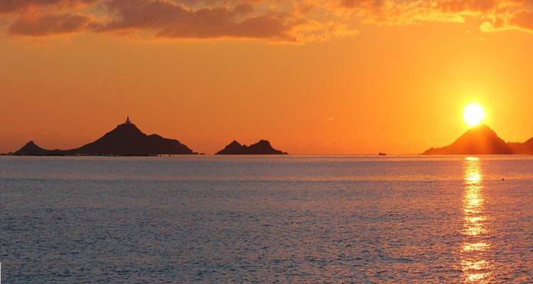 Leuchtend orangefarbener Sonnenuntergang über der Silhouette der Îles Sanguinaires in ruhigen Gewässern des Mittelmeers