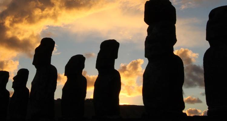 Silueta de una línea de estatuas moai contra dramáticas nubes doradas del atardecer