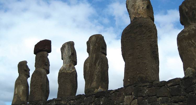 Fila de estatuas moai antiguas dispuestas contra un cielo azul brillante sobre una plataforma de piedra