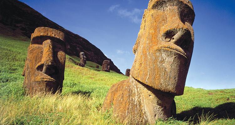 Primer plano de cabezas moai erosionadas parcialmente enterradas en una ladera volcánica cubierta de hierba