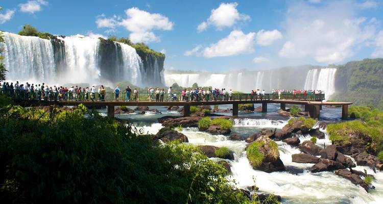 Des foules sur une passerelle en bois face aux multiples rideaux des chutes d'Iguazu sous un ciel bleu