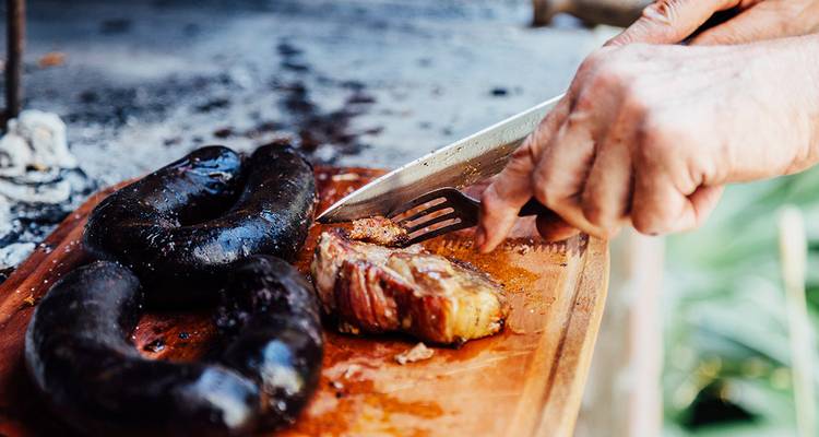 Tabla de madera con morcilla y bife a la parrilla siendo cortados para asado argentino