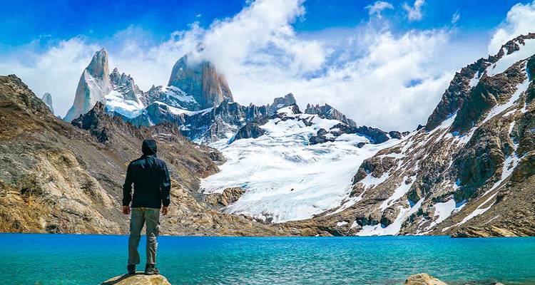 Randonneur debout sur un rocher surplombant un lac glaciaire turquoise sous les sommets enneigés du Fitz Roy