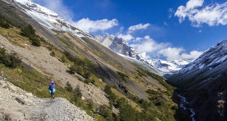 Des randonneurs avec sacs à dos parcourant une vallée patagonienne escarpée avec des sommets enneigés au-dessus
