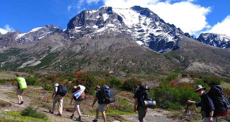 Un groupe de randonneurs avec des sacs à dos marchant le long d'un sentier rocheux avec une montagne enneigée spectaculaire qui se dresse derrière eux.