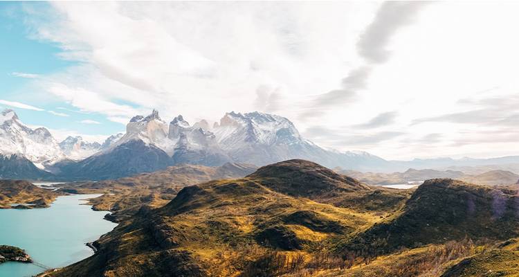 Large panorama aérien de pics escarpés s'élevant au-dessus de lacs turquoise et de collines ondulantes en Patagonie.