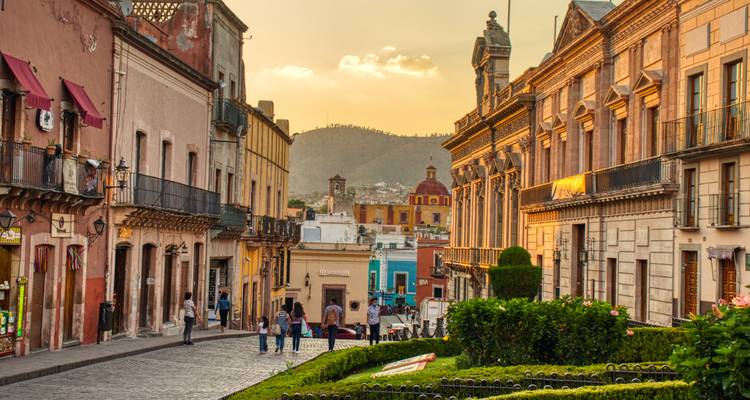 La lumière du couchant baigne une rue coloniale mexicaine aux bâtiments colorés et aux collines lointaines.