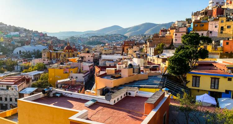Vue panoramique d'une ville mexicaine colorée à flanc de colline avec des montagnes ondulantes au-delà.