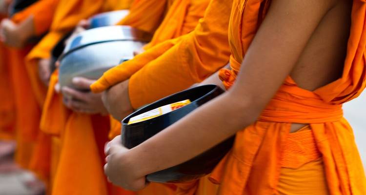 Line of saffron-robed monks holding alms bowls during a ritual procession.