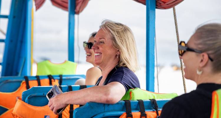 Smiling travellers wearing life-jackets sit on a brightly painted boat.
