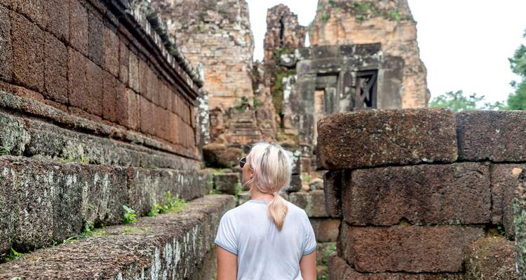 Back view of a traveller exploring moss-covered stone ruins within the Angkor complex.