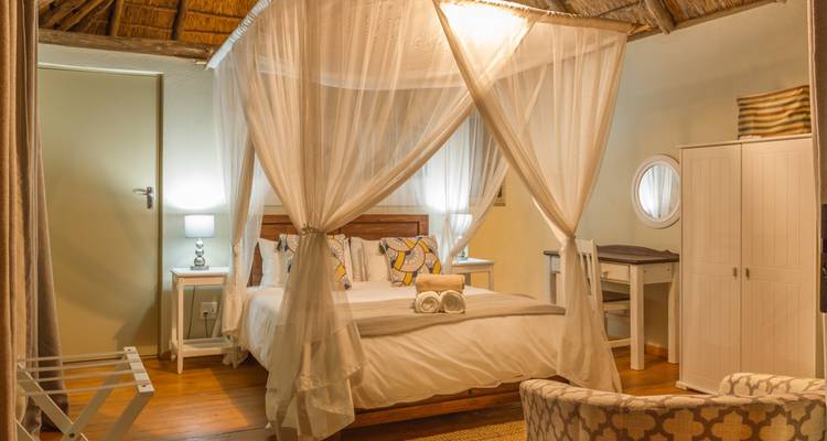 Dormitorio acogedor de lodge de safari con techo de paja y una cama con dosel de gasa.