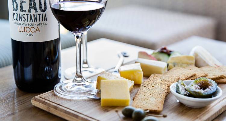 Tabla de quesos con higos, alcaparras y una copa de vino tinto sobre una tabla de madera.