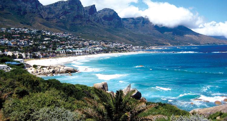 Bahía turquesa espectacular bordeada por rocas con la cadena montañosa de los Doce Apóstoles detrás.