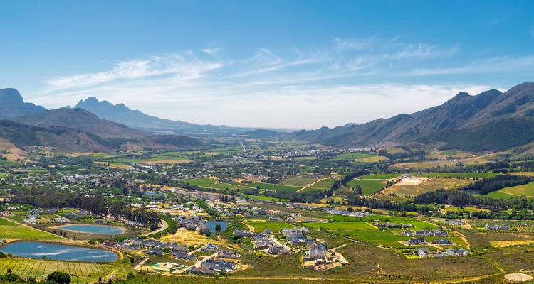 Valle panorámico de viñedos, estanques y pequeños pueblos rodeados por montañas escarpadas bajo un cielo despejado.