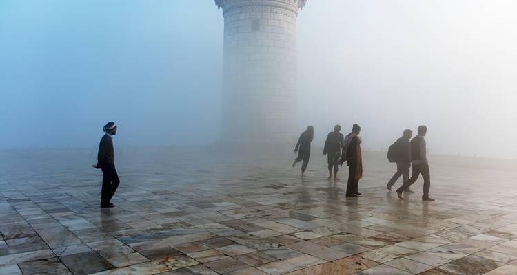 Figuras deambulan por un patio de mármol envuelto en niebla junto a un minarete imponente.