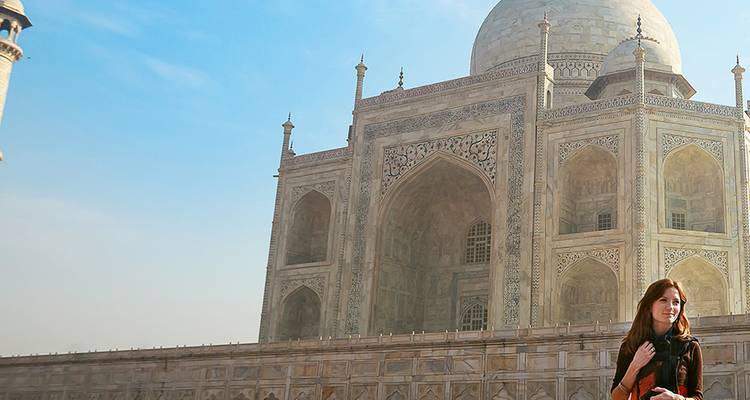Viajero sonriente posa frente a las cúpulas y arcos de marfil del Taj Mahal bajo el cielo azul.