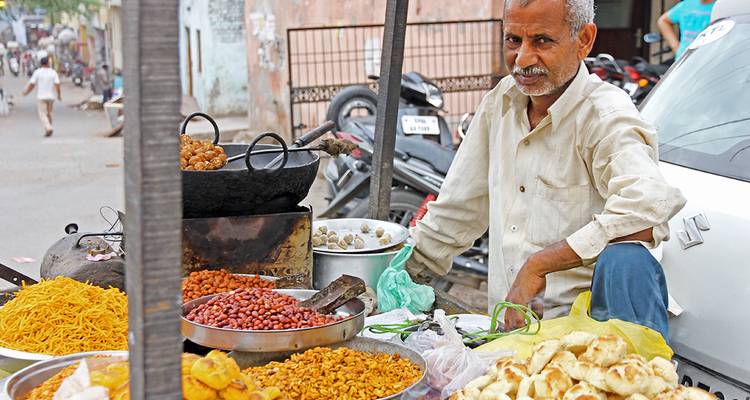 Un vendedor ambulante vende una variedad de bocadillos coloridos y comidas fritas desde un carrito.