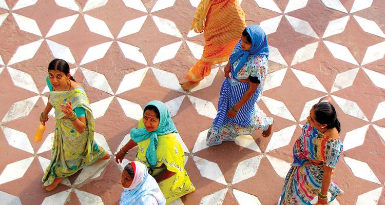 Mujeres con saris coloridos caminan por un patio de piedra con patrones visto desde arriba.