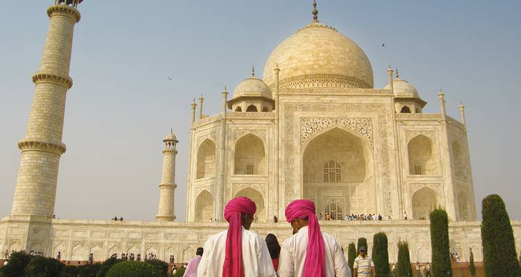 Dos hombres con turbantes rosa brillante caminan hacia la majestuosa fachada de mármol blanco del Taj Mahal.