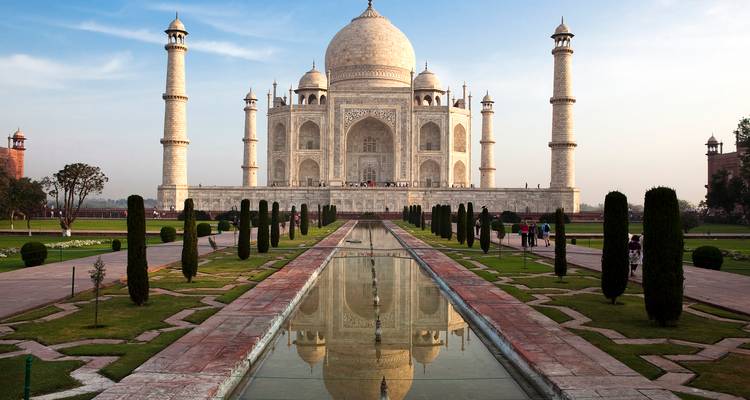 Vista simétrica del Taj Mahal reflejado en el largo canal de agua al amanecer con luz suave.