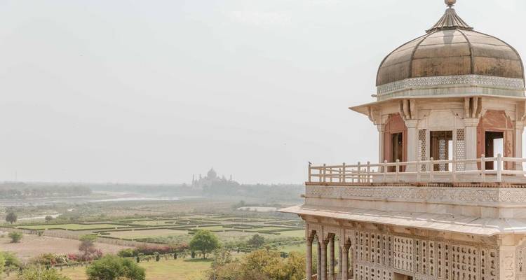 View over Mughal riverside gardens toward distant Taj Mahal framed by an ornate pavilion.