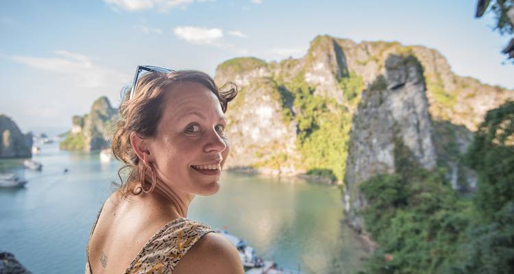 Glimlachende reiziger kijkt achterom vanaf een uitkijkpunt over smaragdgroene wateren en kalkstenen karsten van Ha Long Bay