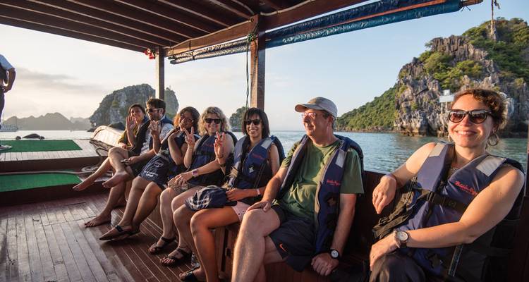 Kleine groep reizigers met reddingsvesten zittend op een houten boot varend tussen karsteilanden