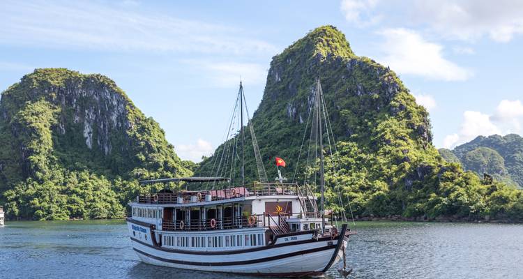 Traditionele houten cruise junk voor anker voor groene kalkstenen kliffen in Ha Long Bay
