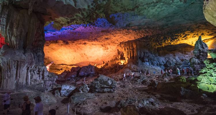 Kleurrijk verlichte grotinterieur met stalactieten en toeristen die de ruime kamer in Ha Long Bay verkennen