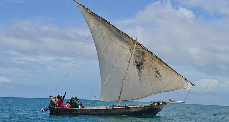 Crew on a traditional dhow raising its large triangular sail in open sea.