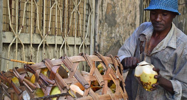 Local vendor cutting open a fresh coconut beside a woven basket of husks.